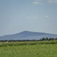 Łagodne, zalesione góry świętokrzyskie szczyty na horyzoncie, z zielonym polem na pierwszym planie.