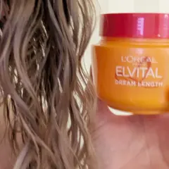 En hand håller en burk med L'Oréal Elvital Dream Length hårinpackning bredvid blekt, vått hår.