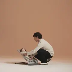 En man justerar en bebis i en BabyBjörn babysitter. Babysittern har flera olika lägen för barnets komfort.