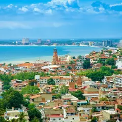 Vista panorámica de una ciudad costera en México, con casas de tejas rojas, una iglesia con cúpula y edificios modernos junto al mar azul. ¡Un sueño para vivir en México!
