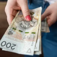 Dłoń trzyma plik banknotów 200 zł. Zastanawiasz się, ile za godzinę pracy?