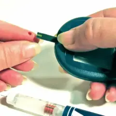Kropla krwi na palcu, pasek testowy i glukometr. Obok wstrzykiwacz z insuliną aspart sanofi.