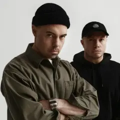 Dwóch mężczyzn, jeden w czarnej czapce beanie i oliwkowej koszuli, drugi w czarnej czapce z daszkiem. Zapowiedź nowych pro8l3m albumy.