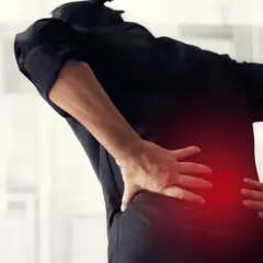 Osoba w czarnej bluzce odczuwa silne drętwienie pleców, trzymając się za bolący odcinek lędźwiowy.