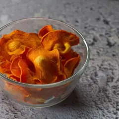 Croccanti chips di carote, preparate in friggitrice ad aria, servite in una ciotola di vetro.