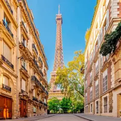 Vue sur la Tour Eiffel entre deux immeubles parisiens, un jour férié de mai. Les balcons ornés et les façades en pierre rappellent le charme de la capitale.