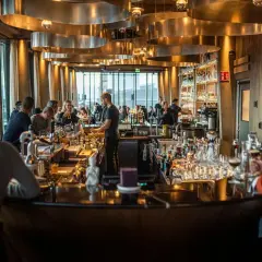 Människor sitter vid en bar med många flaskor och glas. Belysningen är varm och stämningen inbjuder till att läsa **spesso recensioner** om stället.