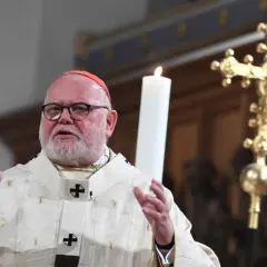 Kardinal Marx spricht in festlicher Robe vor einer Kerze und einem goldenen Kreuz.