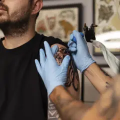 Artysta w rękawiczkach tworzy tatuaż na ramieniu klienta. To moment, by dowiedzieć się, jak zacząć tatuować profesjonalnie.