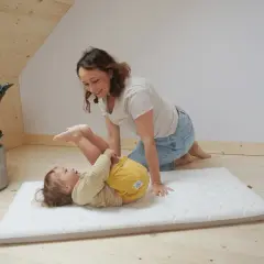 Mama bawi się z dzieckiem na materacu. Czy do łóżeczka turystycznego potrzebny jest materac? Tak, dla komfortu malucha.