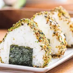 Triangular onigiri rice balls, coated in furikake seasoning, showcase the best rice for onigiri. A piece of nori seaweed adorns the front.