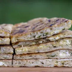 Pile de pains plats au fromage et aux herbes, rappelant l'origine du cheese naan.