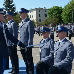 Uroczyste mianowanie na nowych zasadach. Policjanci w galowych mundurach, jeden klęczy, otrzymując szablę.