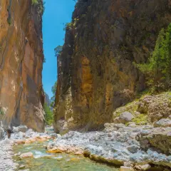 Wanderer in der Samaria Schlucht, umgeben von steilen Felswänden und einem klaren Flussbett.