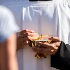 Kapłan w białej albie trzyma złoty kielich z hostią. Czy po masturbacji można iść do komunii? To pytanie nurtuje wielu wiernych.