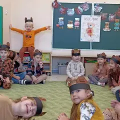 Dzieci w strojach misiów siedzą na dywanie w sali przedszkolnej.