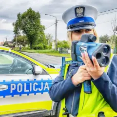 Policjantka z radiowozem i taryfikatorem mierzy prędkość na drodze.