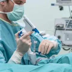 Chirurg w masce i rękawiczkach przygotowuje się do biopsji prostaty, trzymając specjalistyczny przyrząd.