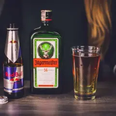 Butelka Red Bull i Jägermeister obok szklanki z drinkiem. Idealny zestaw na imprezę.