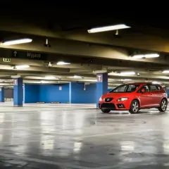 Czerwony samochód na pustym parkingu podziemnym. W tle tablica "Wyjazd". Myśląc o opłatach za garaż we wspólnocie mieszkaniowej, warto pamiętać o takich miejscach.