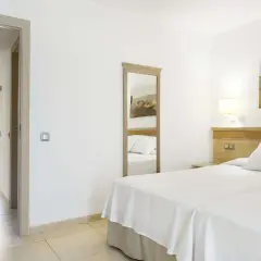 Habitación luminosa en Iberostar Club Cala Barca con dos camas, espejo de cuerpo entero y acceso a un patio exterior.