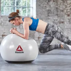 Kobieta w sportowym stroju wykonuje ćwiczenie w podporze na piłce Reebok.