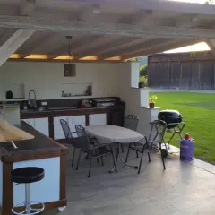 Gemütlicher **Grillplatz im Garten** mit Außenküche, Tisch und Stühlen unter einem Holzüberdach. Perfekt für Sommerabende.