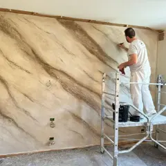 Pittore applica stucco effetto marmo su una parete, creando venature naturali.