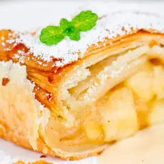 Ein Stück Apfelstrudel mit Puderzucker und Minze, serviert mit Vanillesauce. Perfekt für ein Apfelstrudel Rezept!
