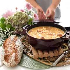 Un reconfortante plato de callos a la gallega humea en una cazuela, acompañado de pan rústico y un ramo de flores.
