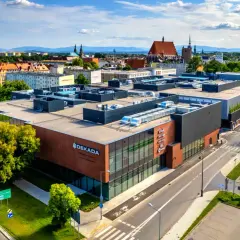 Nowoczesny budynek usługowy "Dekada" z przeszkloną fasadą i ceglanymi elementami, otoczony zielenią i drogami.