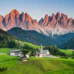 A picturesque village nestled in a valley, with the jagged peaks of the Dolomites catching the golden light, a stark contrast to the gentler slopes of the Alps.