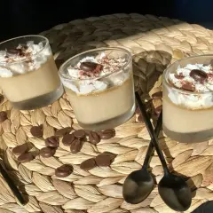 Trois verrines de crème au café facile, garnies de chantilly, cacao et grains de café. Des chocolats en forme de grains parsèment le napperon.