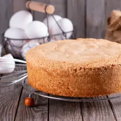 Puszysty biszkopt z olejem, gotowy do dekoracji. Obok jajka, mąka i trzepaczka.
