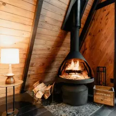 Gemütlicher Kaminofen mit Zulassung, bereit für den Schornsteinfeger. Holzscheite liegen daneben.