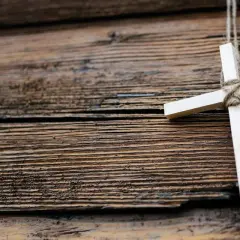 Ein hölzernes Kreuz, gebunden mit Seil, hängt vor einer rustikalen Holzvertäfelung. Ein Symbol für den Karfreitag, den Feiertag der Besinnung.
