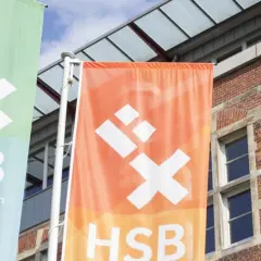 Zwei Fahnen der Hochschule Bremen City University of Applied Sciences wehen vor einem Backsteingebäude.