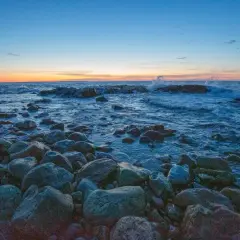 Stenstrand vid solnedgången. Vågor slår mot klipporna i det blåa vattnet. En lugn kväll, precis som det iso betyder.
