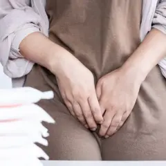 Kobieta zakrywająca intymne okolice, obok stos podpasek. Może to sugerować **infekcja intymna objawy** i dyskomfort.