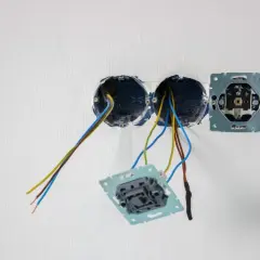 Instalacja elektryczna: puszki, przewody i mechanizmy gniazdek na białej ścianie.