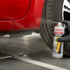Guanto nero spruzza prodotto su auto rossa per togliere il catrame.