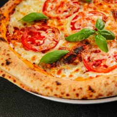 Zbliżenie na domową pizzę z pomidorami, serem i bazylią, z przypieczonym brzegiem.