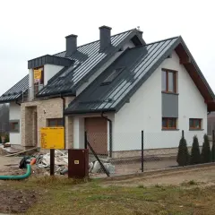 Nowy dom w budowie, widoczny przyłącze napowietrzne, plac budowy z piaskiem i materiałami.