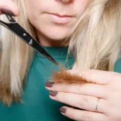 Kobieta z blond włosami podcina końcówki nożyczkami.