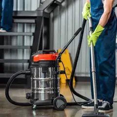 Persona con guantes verdes usa aspiradora industrial, un ejemplo de los tipos de maquinaria de limpieza, junto a escaleras.