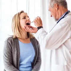 Lekarz bada gardło pacjentki. To ważny krok w diagnozowaniu, czy potrzebny jest urlop zdrowotny dla kogoś, kto źle się czuje.