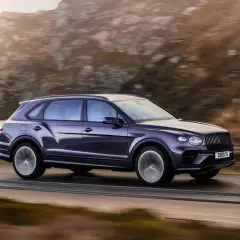 Fioletowy Bentley SUV pędzi po górskiej drodze, otoczony jesiennym krajobrazem.