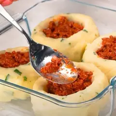 Łyżka nakłada mięsne nadzienie do ziemniaczanych łódeczek. Pyszne dania z ziemniaków w szklanym naczyniu.