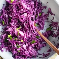 Insalata fresca di cavolo rosso, tagliato finemente e condito con erbe aromatiche, servita in una ciotola con un cucchiaio di legno.