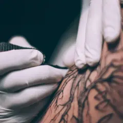 Dłoń w rękawiczce tworzy tatuaż metodą handpoke. To precyzyjne, ręczne tatuowanie, które daje unikalne efekty.